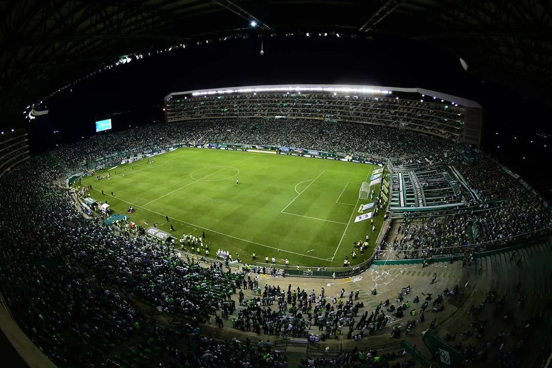 Vista panorámica nocturna del Estadio Deportivo Cali con espectadores en las tribunas y un partido de fútbol en la cancha, fotografiada en 2024.