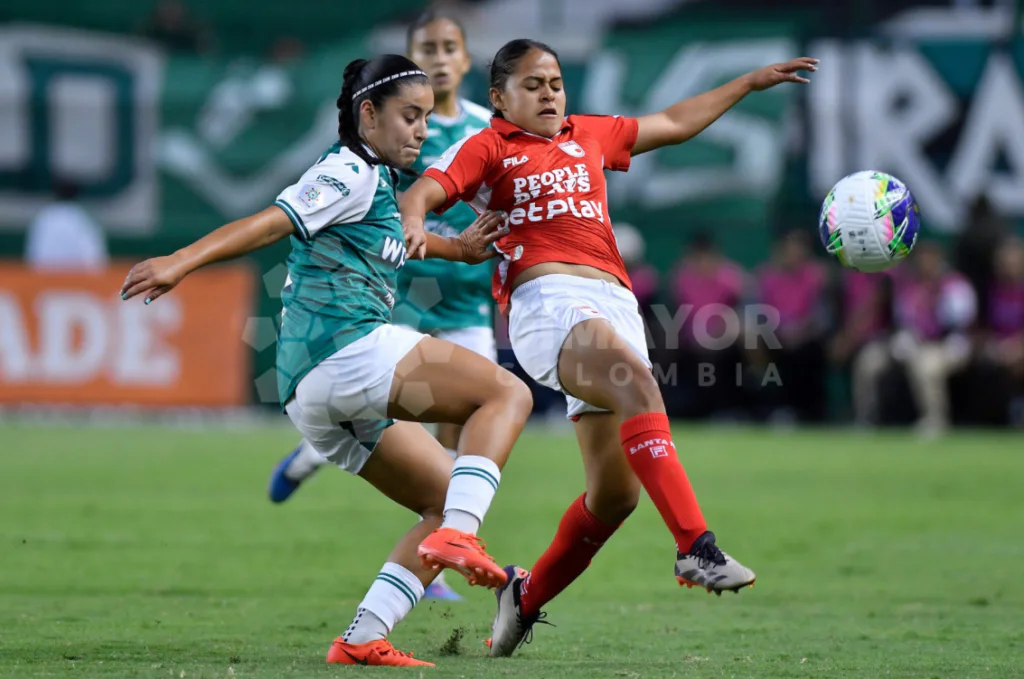 Una jugadora de Independiente Santa Fe, con camiseta roja, disputa el balón frente a una futbolista del Deportivo Cali vestida de verde y blanco.